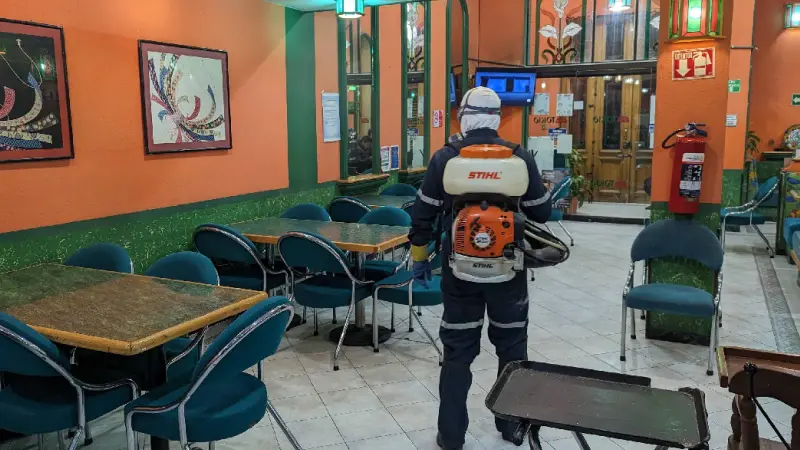 Fumigador profesional dentro de un restaurante caminando entre mesas en busca de plagass